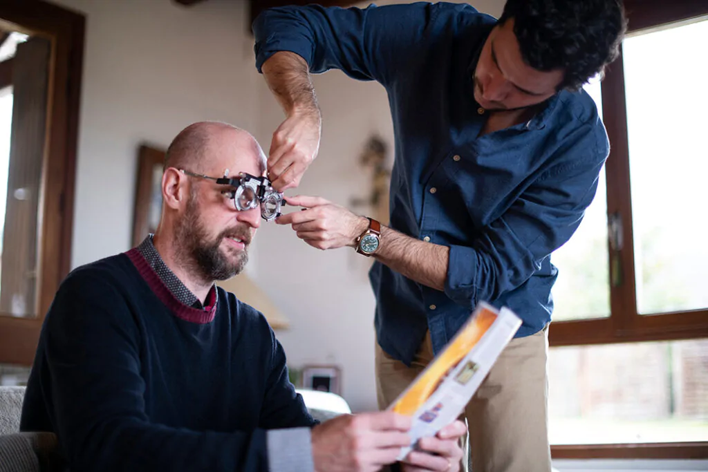Un client teste sa vue avec des lunettes d'essai lors de la visite d'un opticien à domicile.